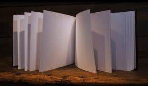 Blank sketchbook standing upright open in the middle with pages flowing to each side gently lit and standing on a warm wooden surface.