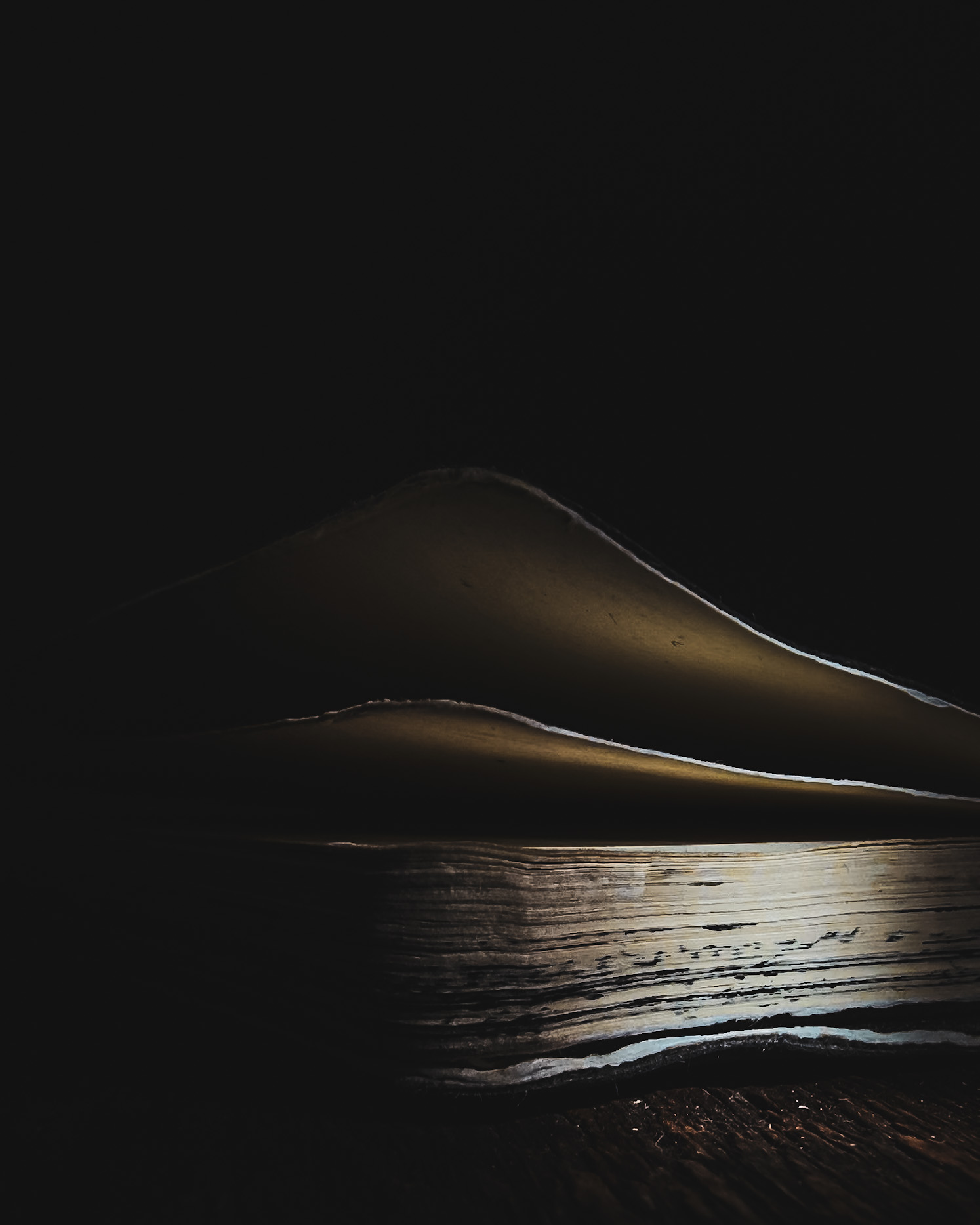 Well-Worn Notebook Corner Moody close-up of a well-worn pocket notebook corner, with curled cover and pages, partly in shadow with light revealing the textured paper edge.