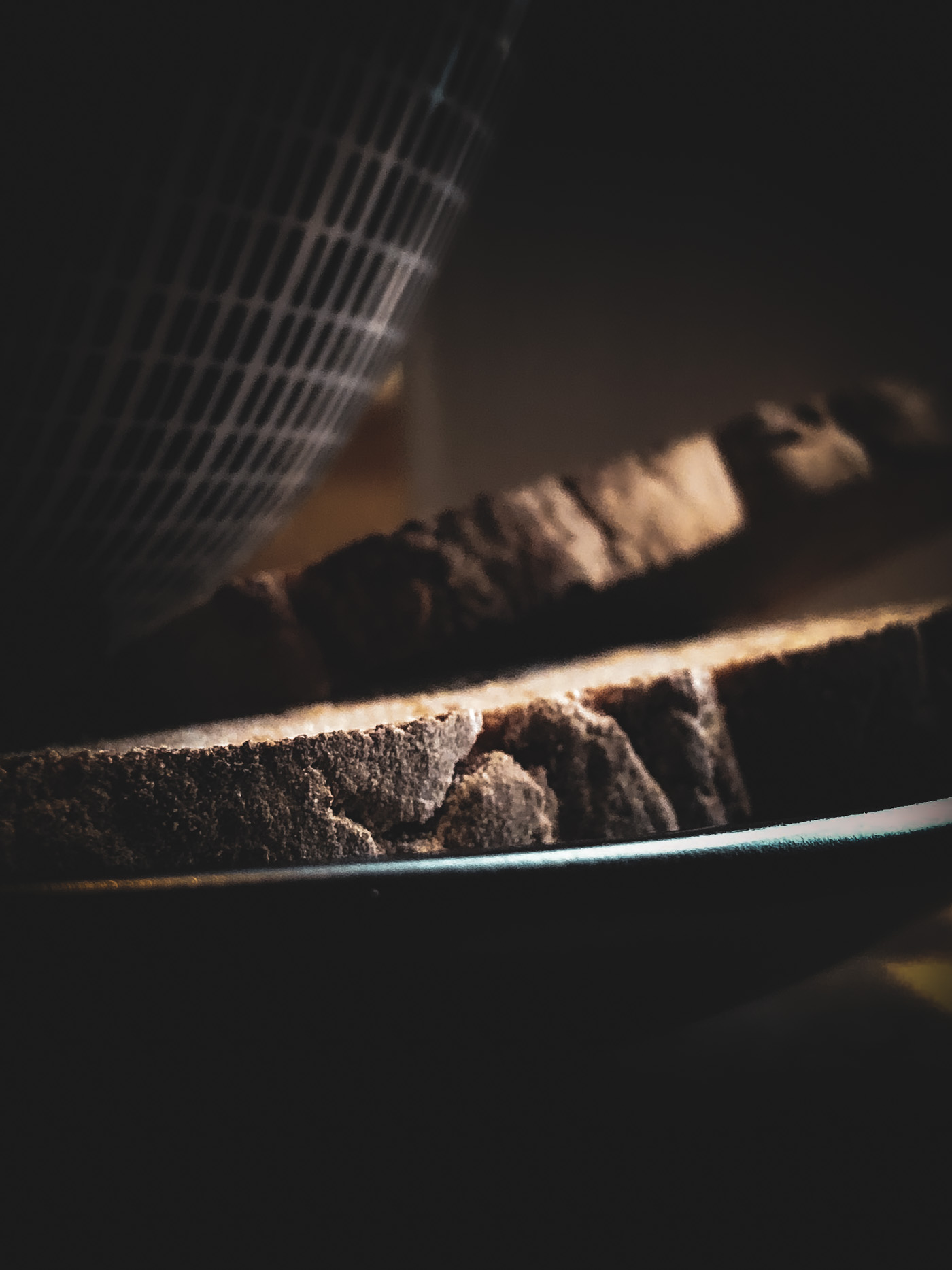 Close-up of sliced rustic bread on a plate, with light highlighting the crust and a bowl of soup softly blurred in the background.