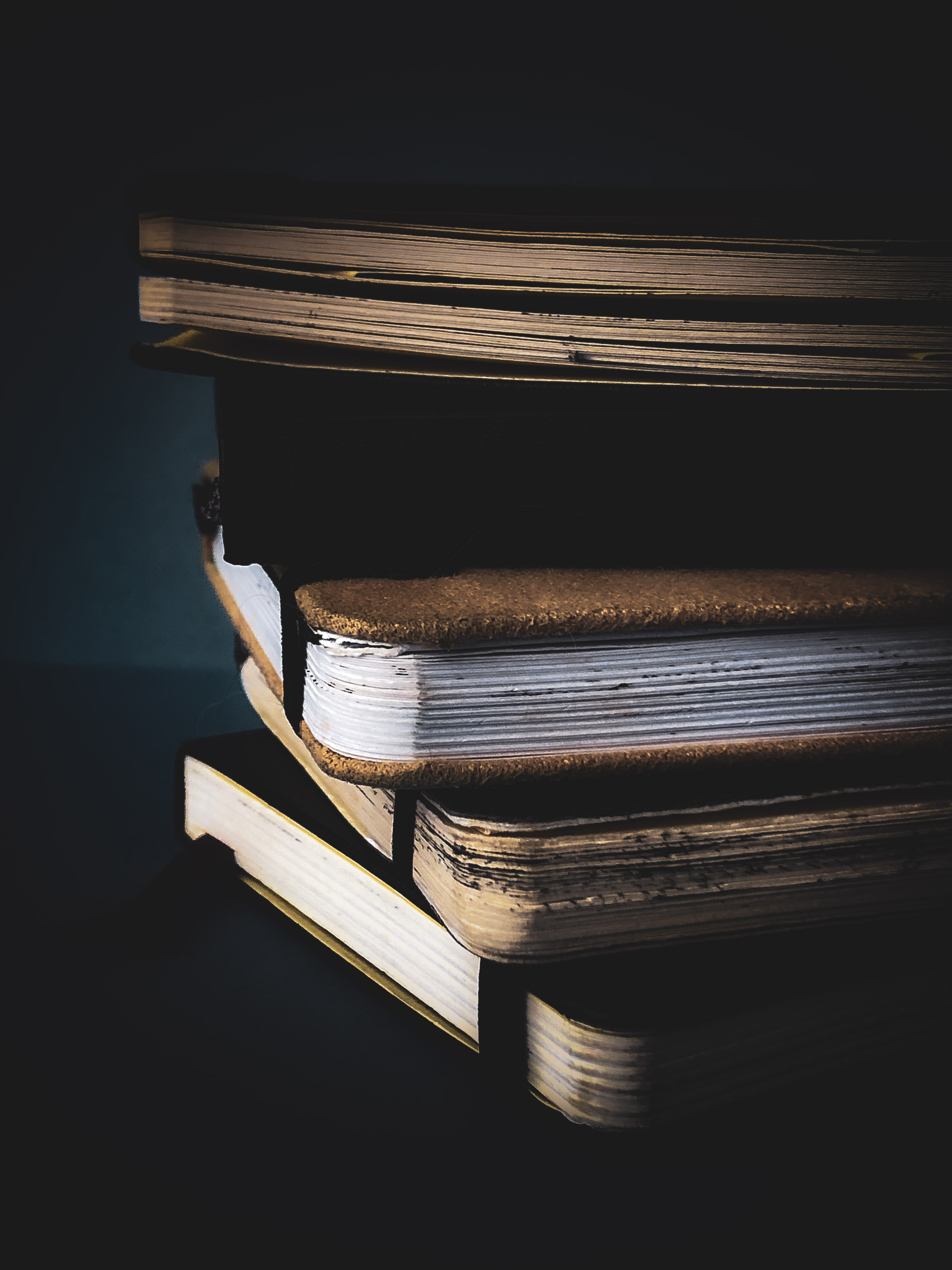 Randomly stacked notebooks in soft light Pile of closed pocket notebooks with varied covers, loosely stacked against a dark background with light catching the edges.