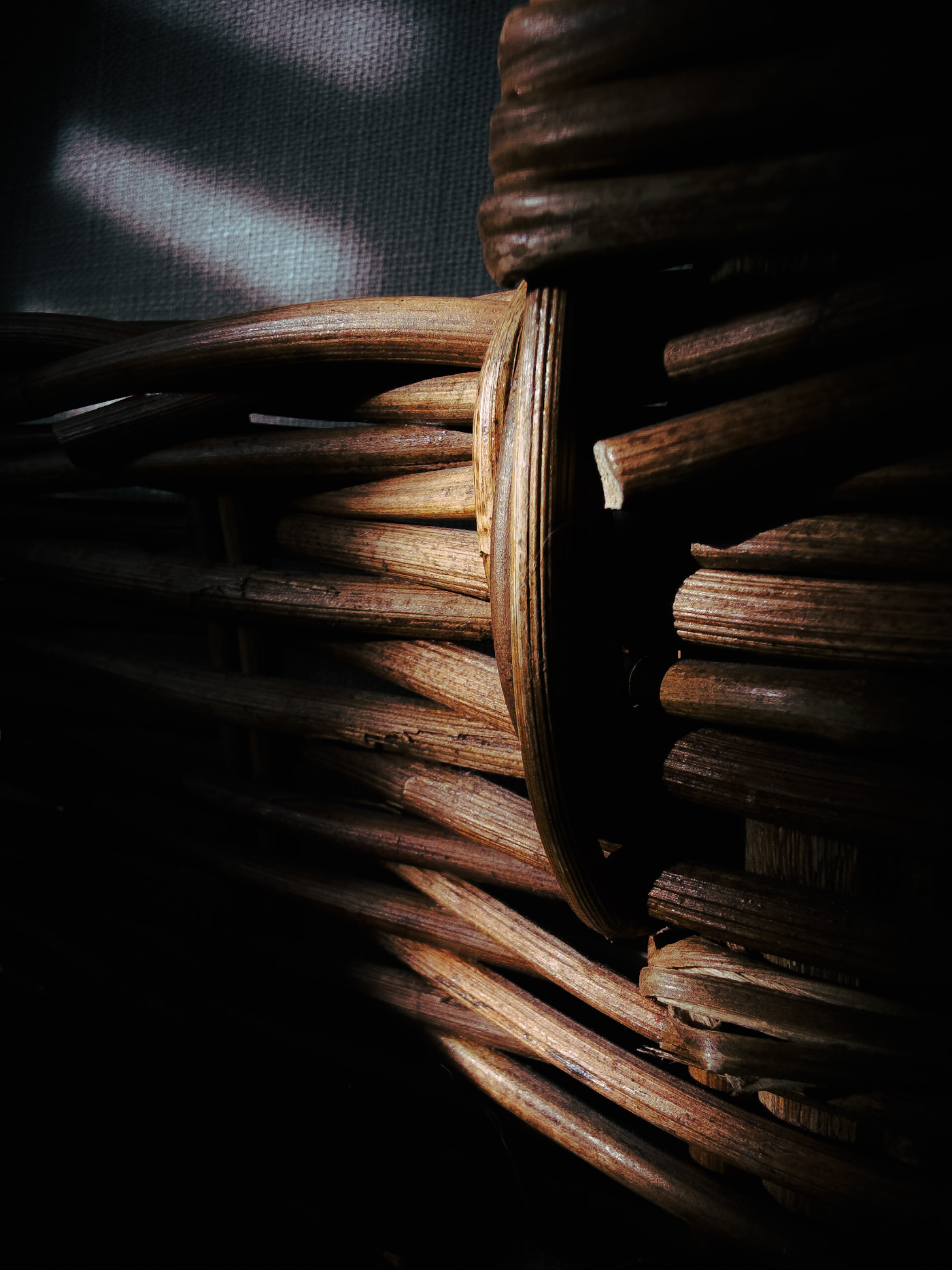 Top view of a wooden bowl filled with mixed nuts, softly revealed by light and partially hidden in shadow