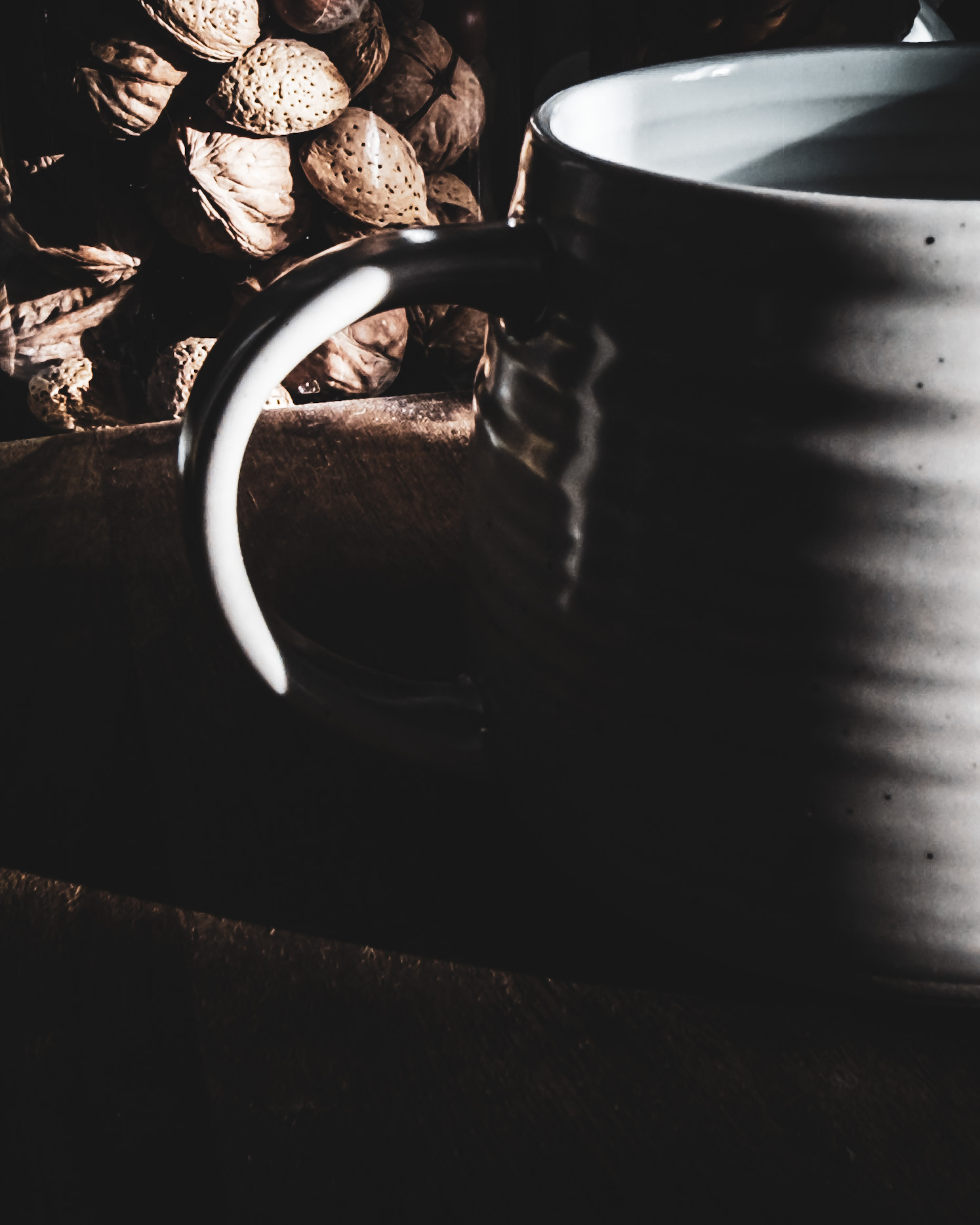 Side view of a mug in dramatic light from the right, with the handle visible and a glass jar of nuts seen in the background through the handle.
