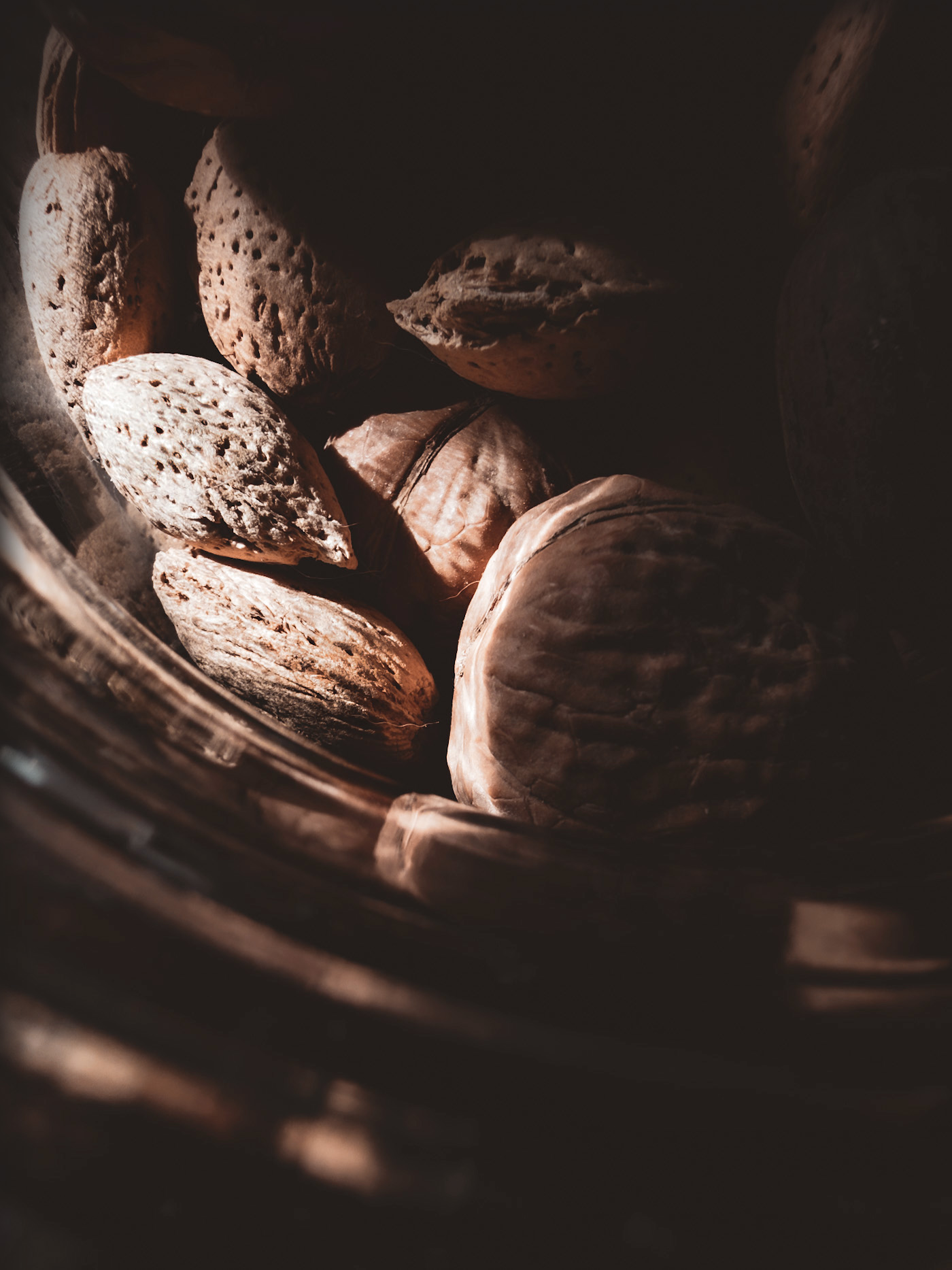 Close-up of a glass jar of nuts, with warm light illuminating some on the left while others remain in shadow.